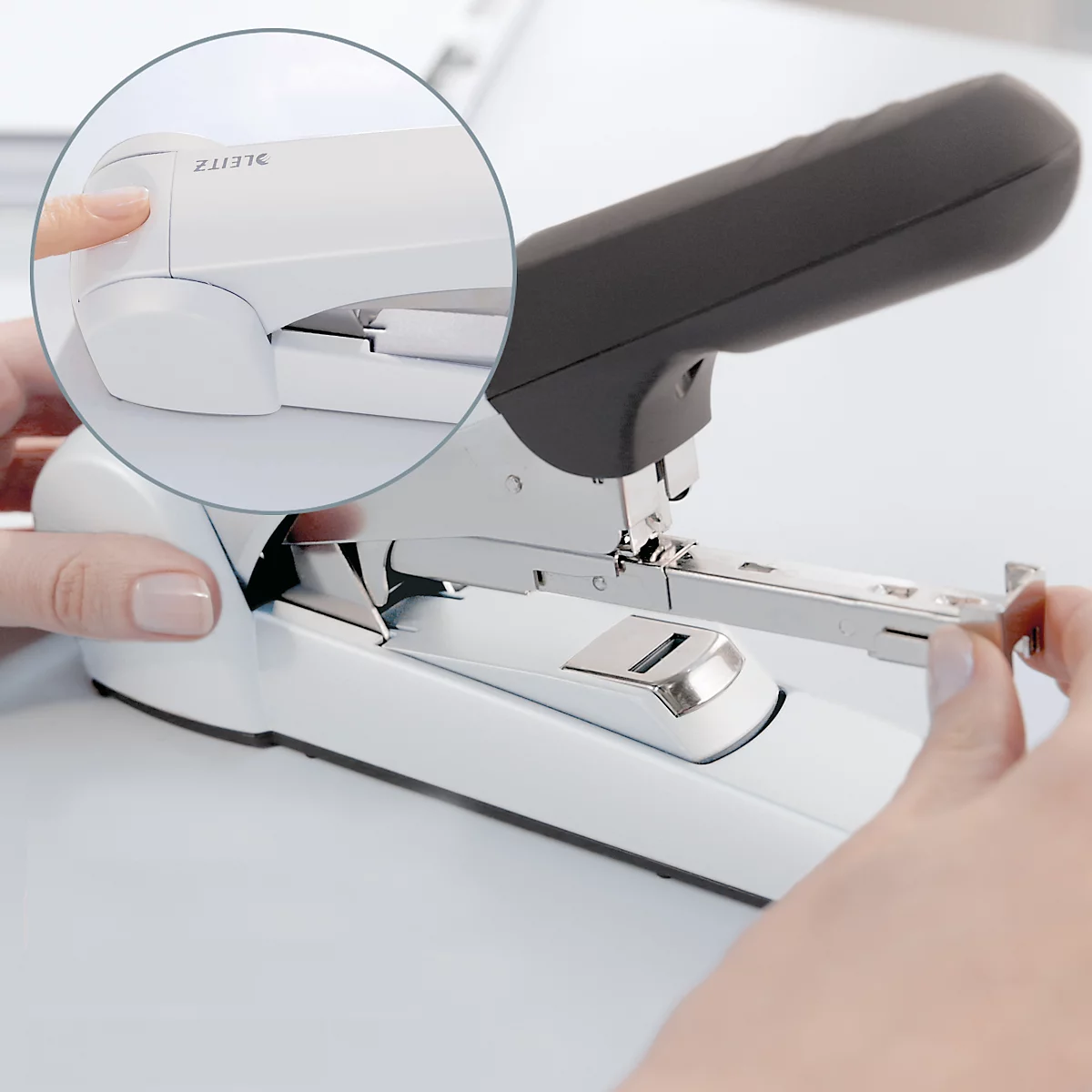 Close-up of a white stapler with a detail cut-out. Person presses a button. The black handle is visible.