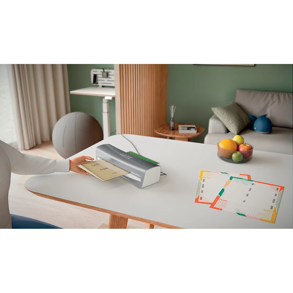 Eine Person laminiert ein Dokument auf einem Tisch. Auf dem Tisch sind Obst und laminierte Vorlagen zu sehen.