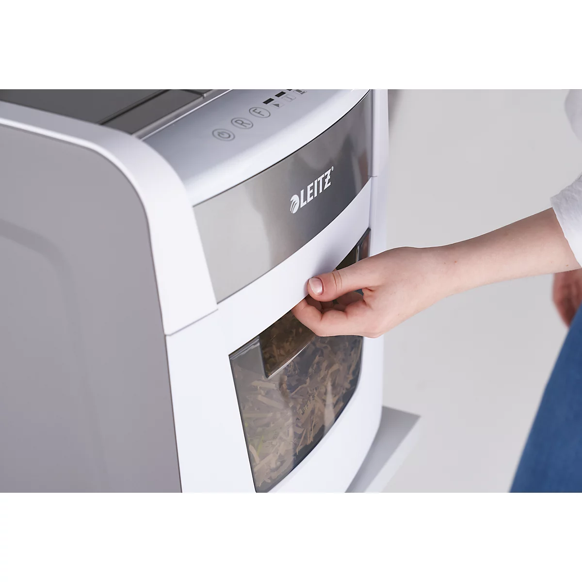 A hand opening a paper tray on a white shredder. The Leitz logo is visible.