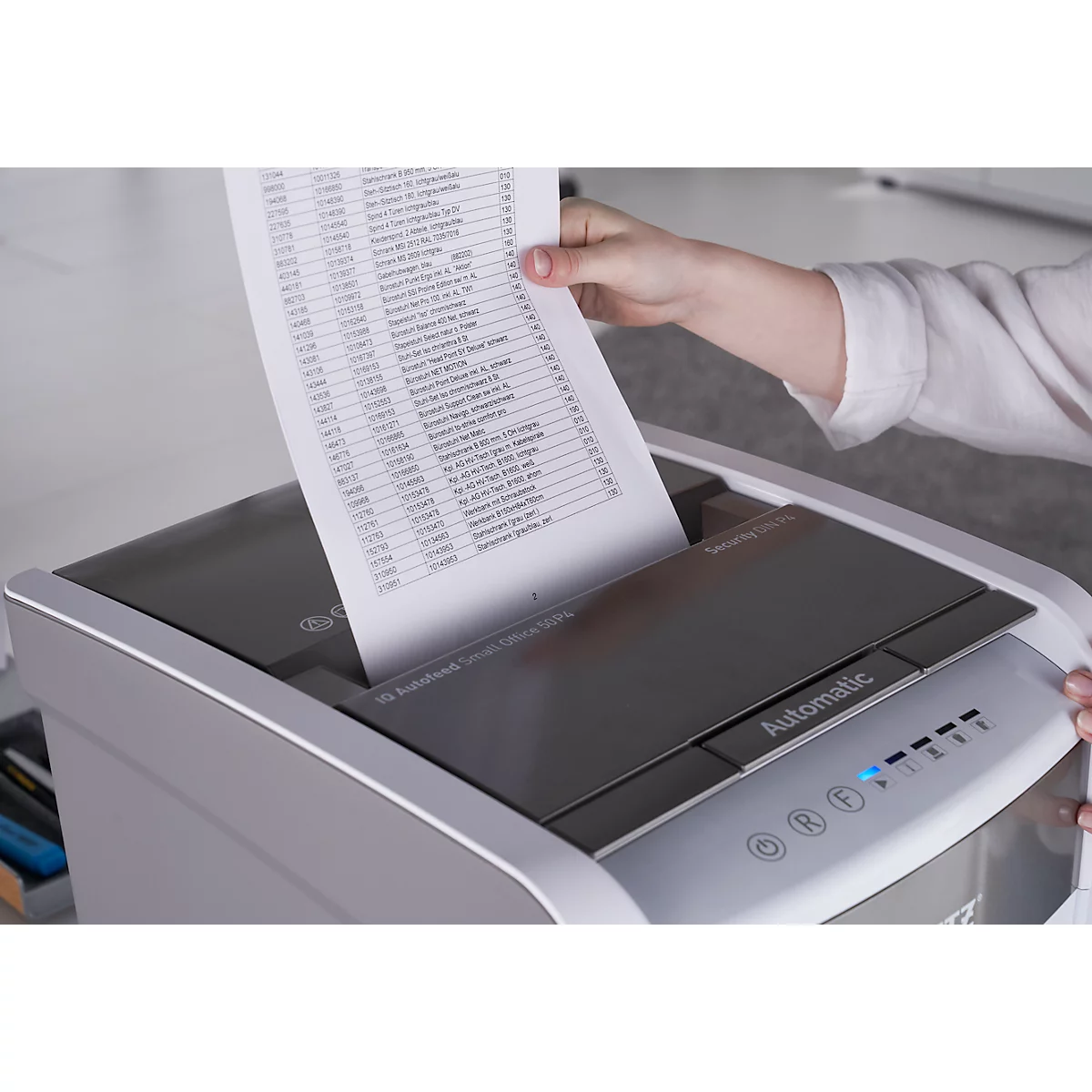 A person is placing a sheet of paper with text into a paper shredder. The shredder is grey, the paper white.