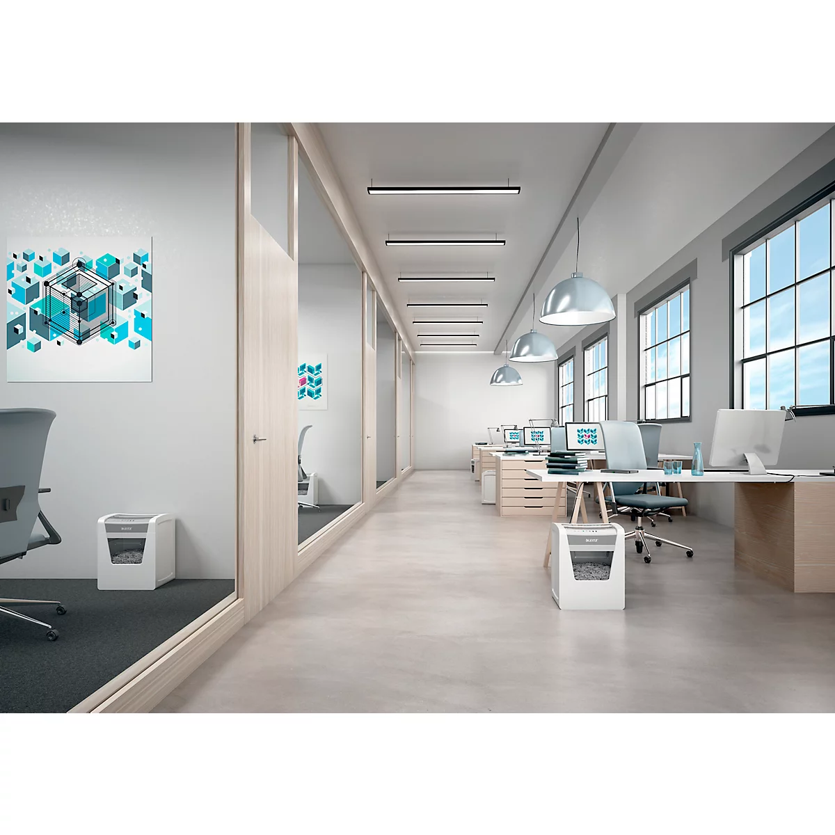 Een kantoorruimte met bureaus, computers, een prullenbak en ramen. Een papierversnipperaar staat op de voorgrond.