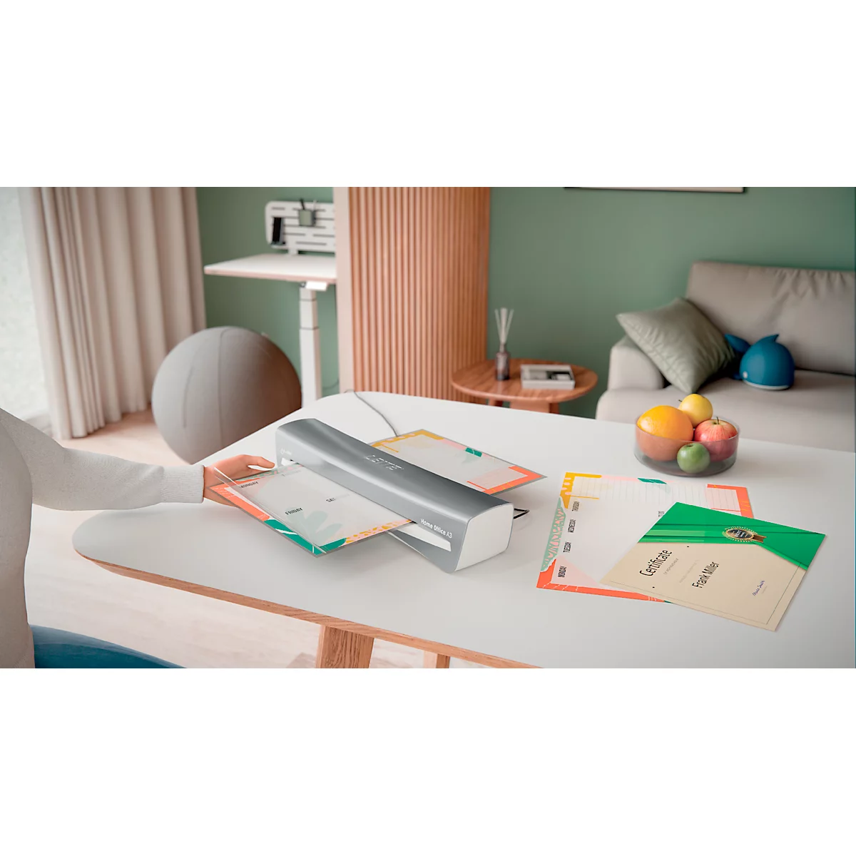 Person laminating paper, with other sheets and fruit on a table. Background: sofa, standing desk.
