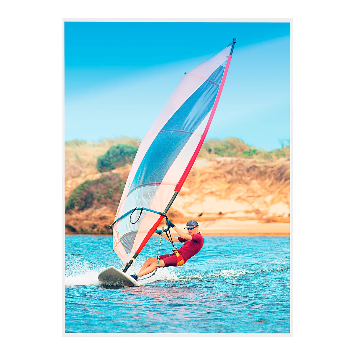 Windsurfer on the water, the sail is white with blue and red accents. The sky is blue.
