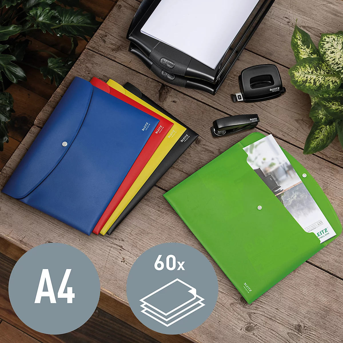 Bunte Dokumentenmappen mit A4-Papier. Auf Holzoberfläche liegen Zubehör wie Locher und Tacker.
