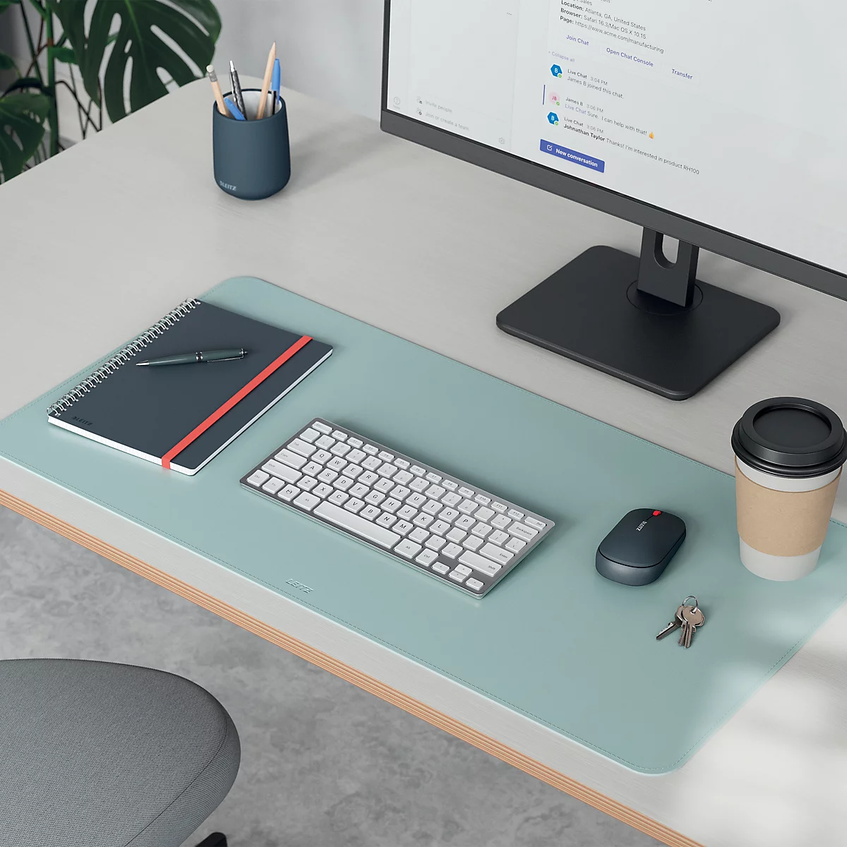 Schreibtisch mit Mauspad, Tastatur, Becher, Notizbuch, Maus, Stifthalter, Monitor, und Schlüssel.