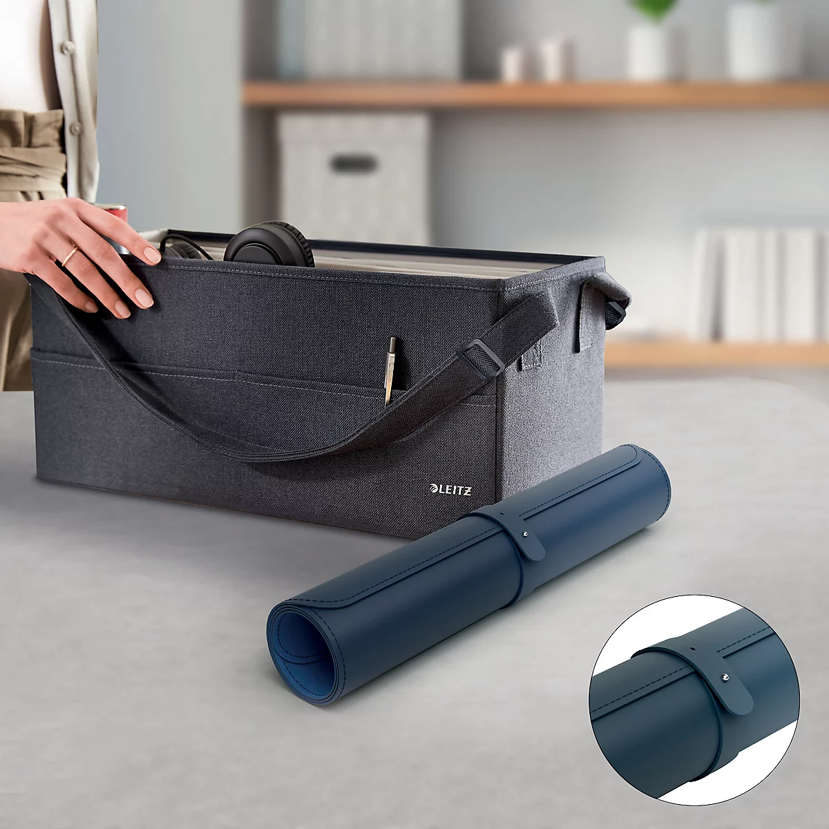 Tapis de bureau roulé bleu foncé avec fermeture en cuir. A côté, une boîte de rangement grise.
