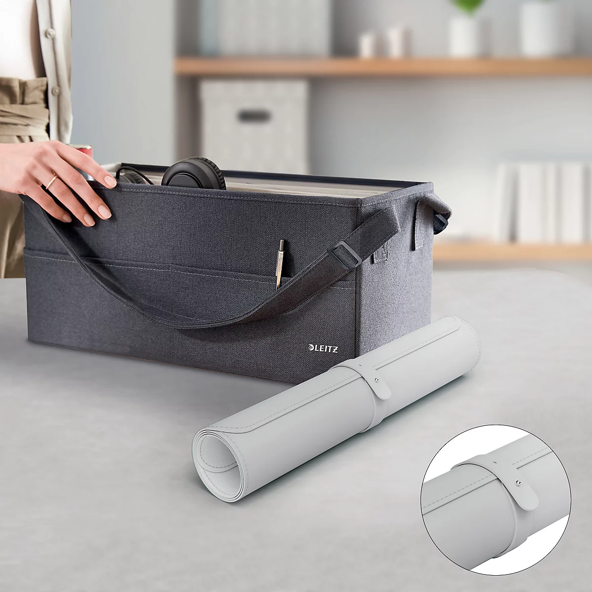 Sac gris avec bandoulière et papier roulé blanc. Une main touche le sac. Vue détaillée du papier fermé.