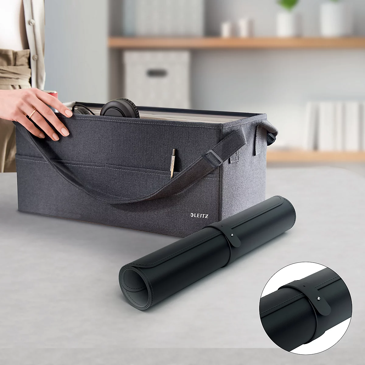 Une personne ouvre un sac en tissu gris avec des poignées. À côté se trouve un tapis de bureau noir enroulé.