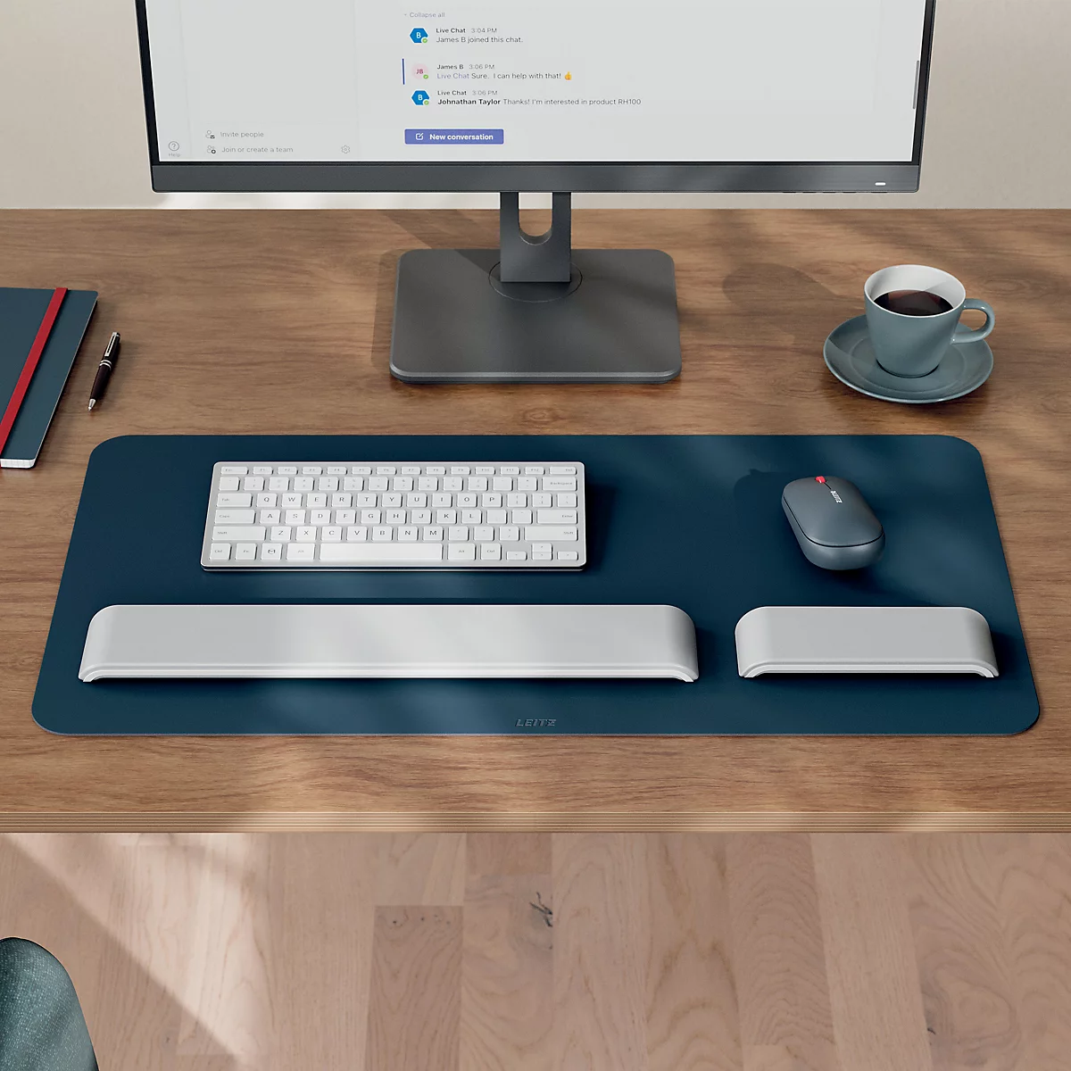 Bureau avec moniteur, clavier, souris et repose-poignets sur un coussin bleu. Une tasse de café se trouve à côté.