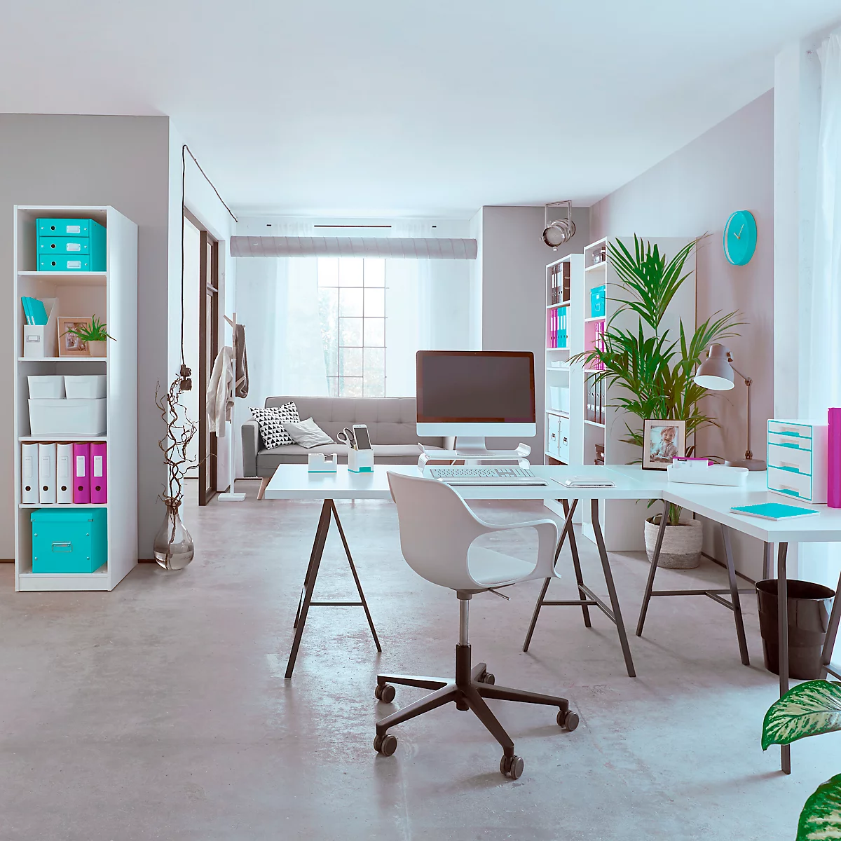 Lichte, moderne werkruimte met bureau, stoel, computer en boekenplank. Een bank is zichtbaar op de achtergrond.