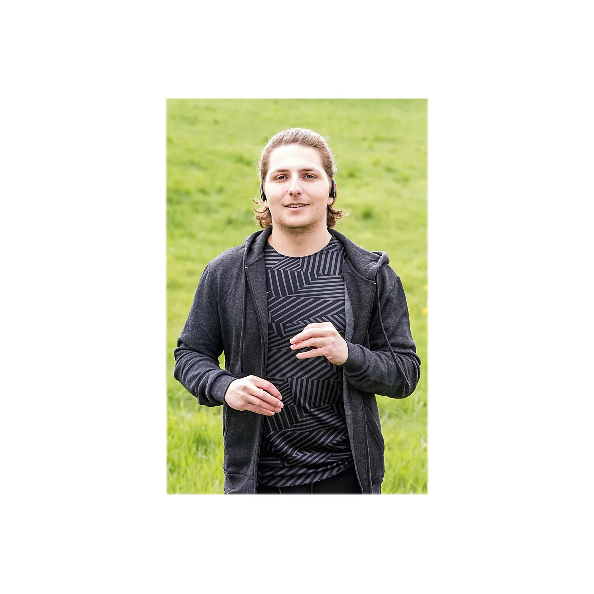 Mann im Jogginganzug mit KopfhÃ¶rern, lÃ¤uft in der Natur. LÃ¤chelt in die Kamera.