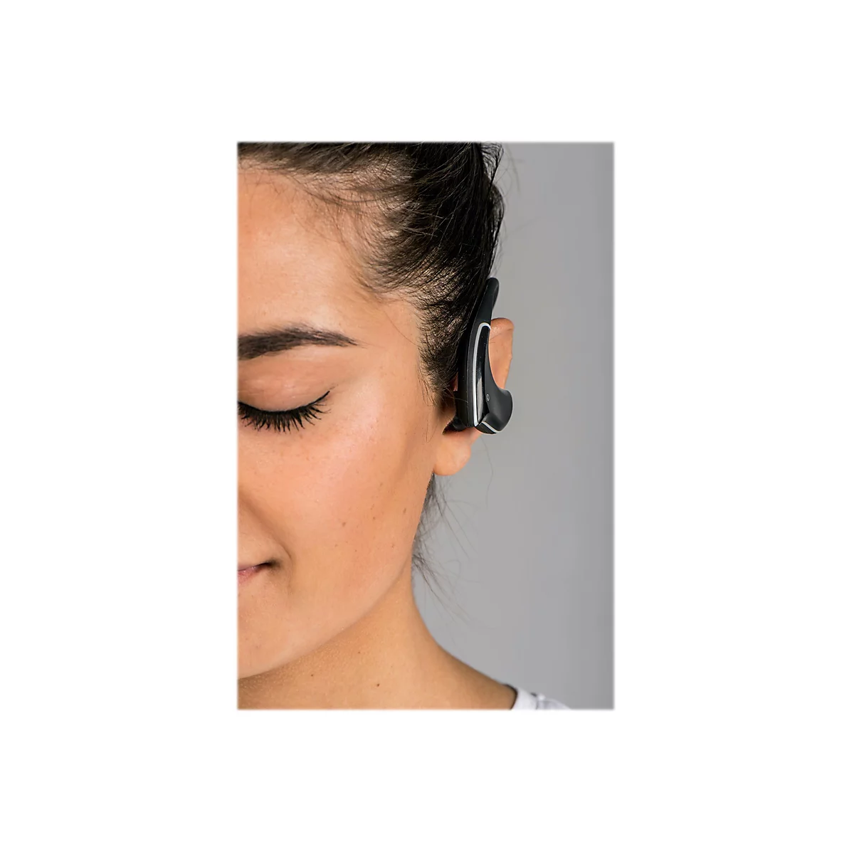 Nahaufnahme einer Frau, die einen schwarzen Bluetooth-KopfhÃ¶rer im Ohr trÃ¤gt. Ihr Auge ist geschlossen, ihr Blick sanft.