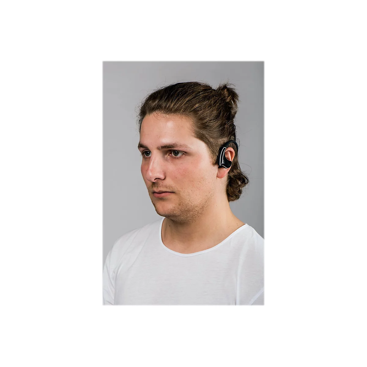Ein Mann mit langen, hochgesteckten Haaren trÃ¤gt einen schwarzen KopfhÃ¶rer im Ohr. Er blickt zur Seite, vor grauem Hintergrund.