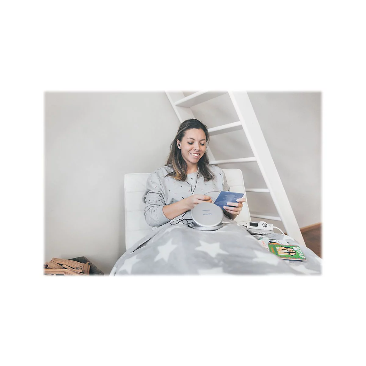 LÃ¤chelnde Frau hÃ¶rt mit KopfhÃ¶rern Musik vom CD-Player im Bett. Decke mit Sternenmuster.