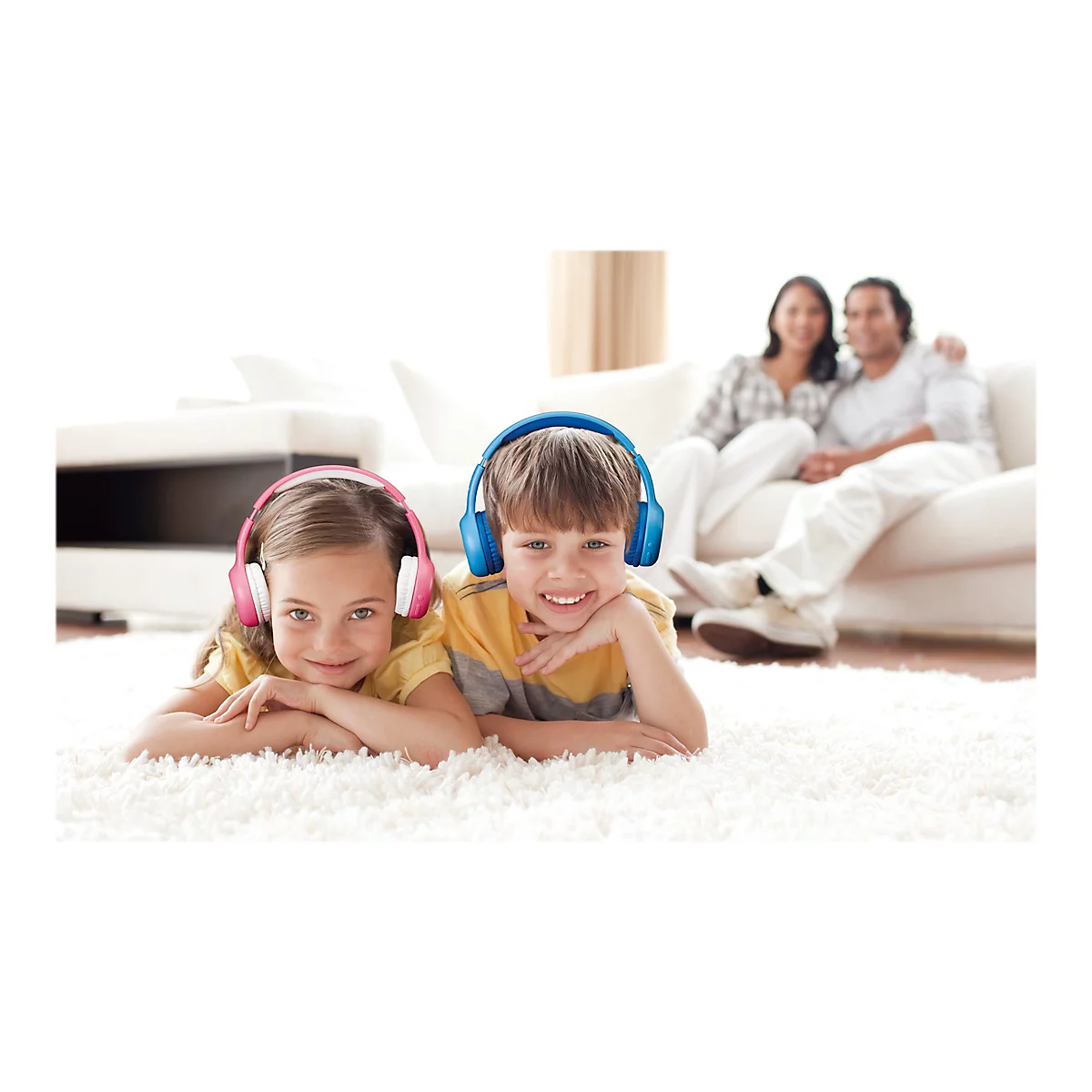 Ein Mädchen und ein Junge liegen auf einem Teppich und hören Musik über Kopfhörer. Im Hintergrund sitzt ein Paar auf einer Couch.