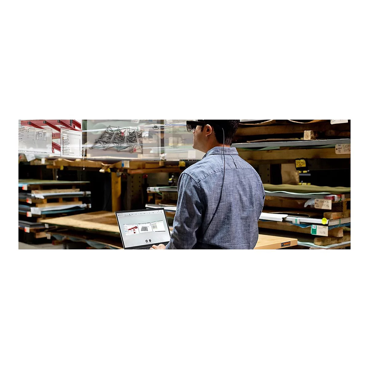 Mann mit AR-Brille vor Laptop, Darstellung einer technischen Zeichnung. Im Hintergrund Holzregale.