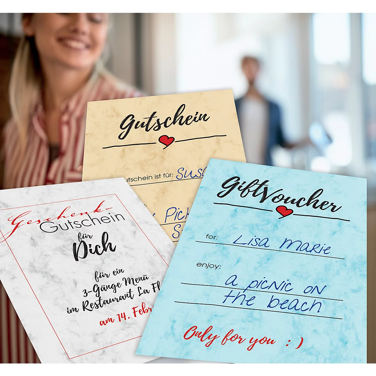 Close-up of three gift vouchers with heart motifs. In the background a smiling woman and a blurred person.