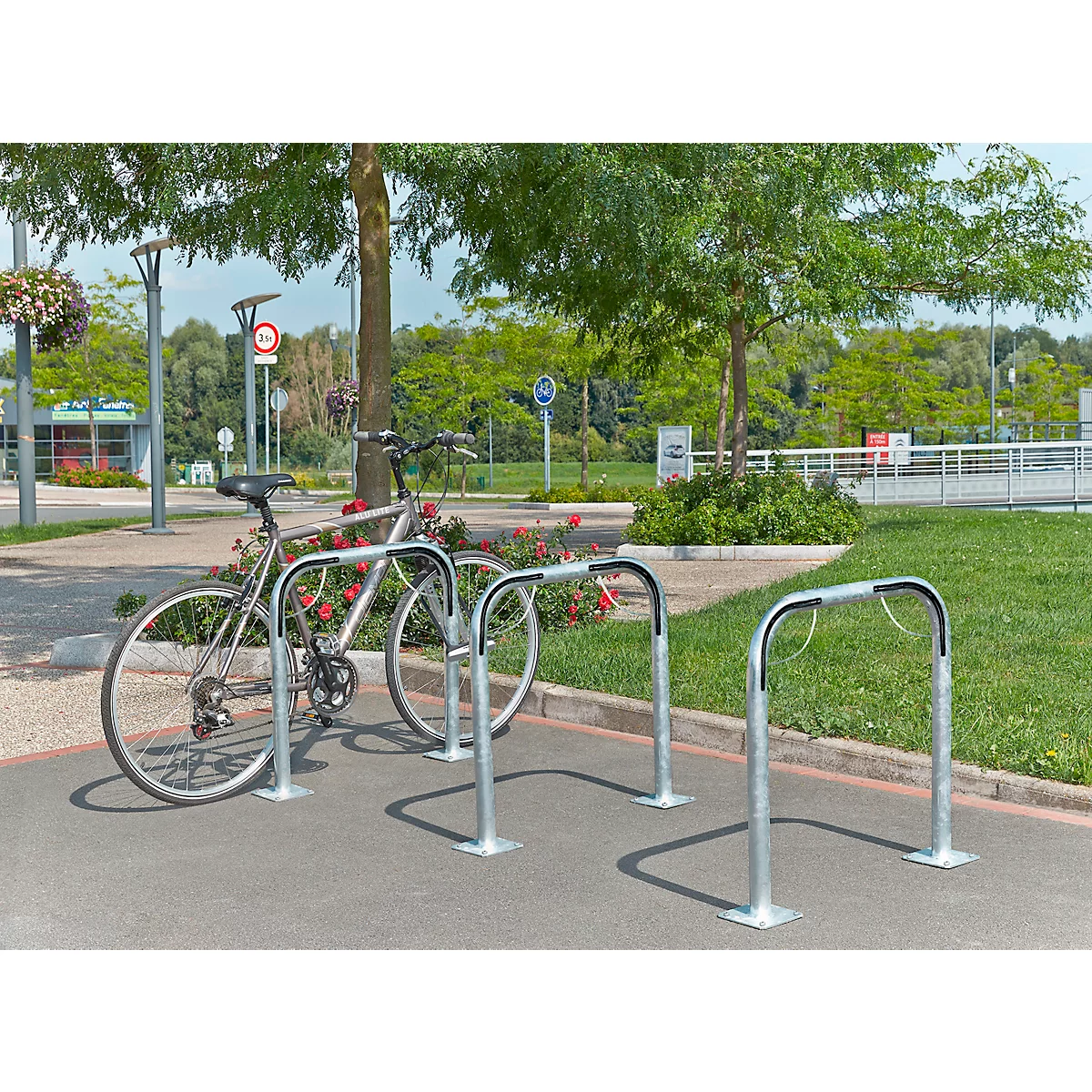 Fiets geparkeerd in fietsenrekken op asfalt, bomen en groene zones op de achtergrond.