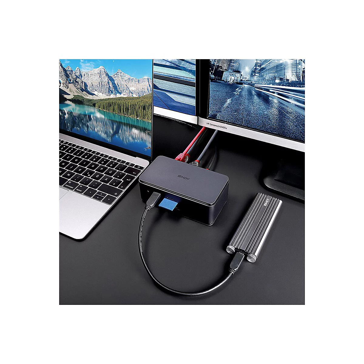Auf einem Schreibtisch sind ein Laptop, zwei Monitore, ein Hub und eine externe Festplatte zu sehen. Beide Bildschirme zeigen unterschiedliche Bilder an.