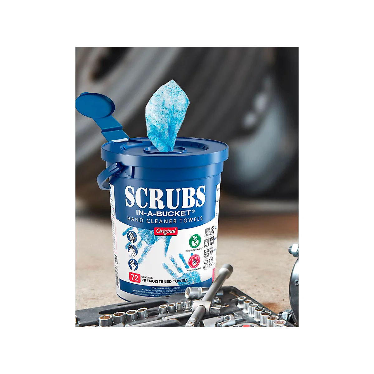 Boîte de lingettes bleues avec l'inscription "SCRUBS". Une lingette dépasse. Outils au premier plan.
