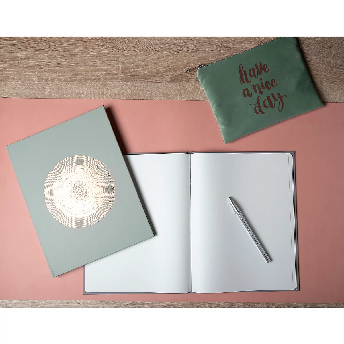 Un carnet avec un décor argenté, un carnet ouvert avec un stylo, un sac vert avec lettrage.