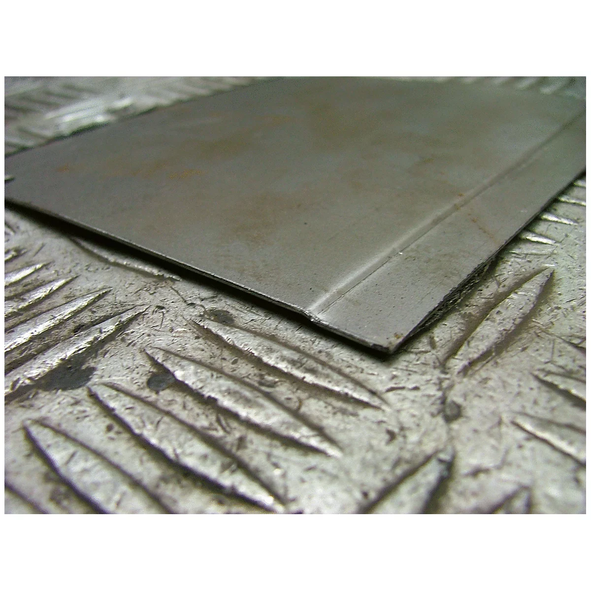 Nahaufnahme eines Metallblechs. Die Oberfläche ist matt, mit einer geprägten, diamantförmigen Textur.