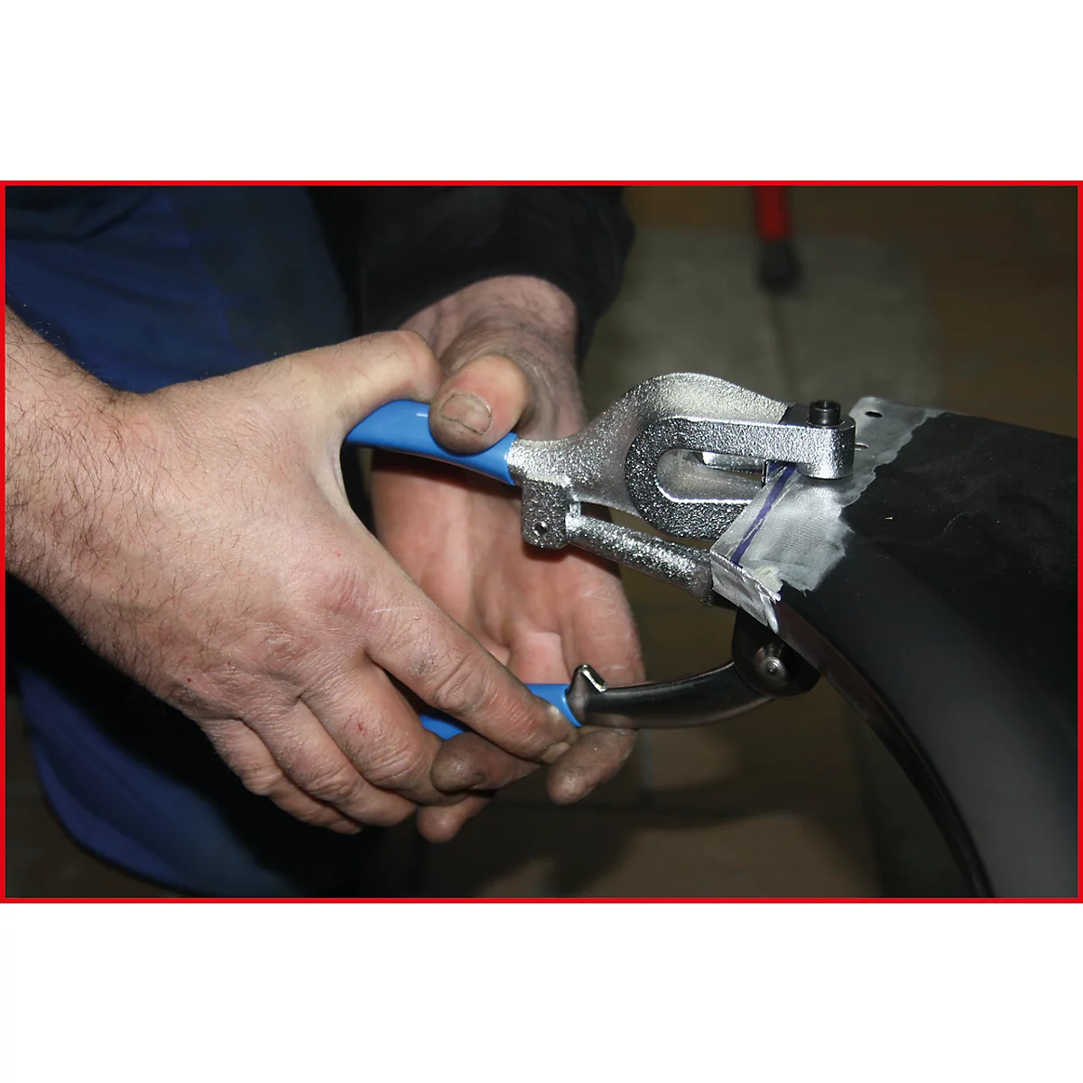 Eine Person benutzt eine Zange mit blauen Griffen, um an einem schwarzen Objekt zu arbeiten.