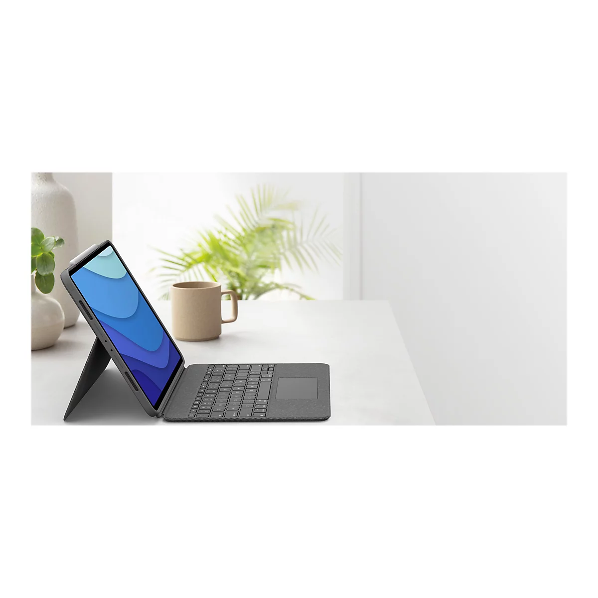 Ein Tablet mit Tastatur steht auf einem Tisch. Im Hintergrund sind eine Tasse, Pflanzen und ein Fenster zu sehen.
