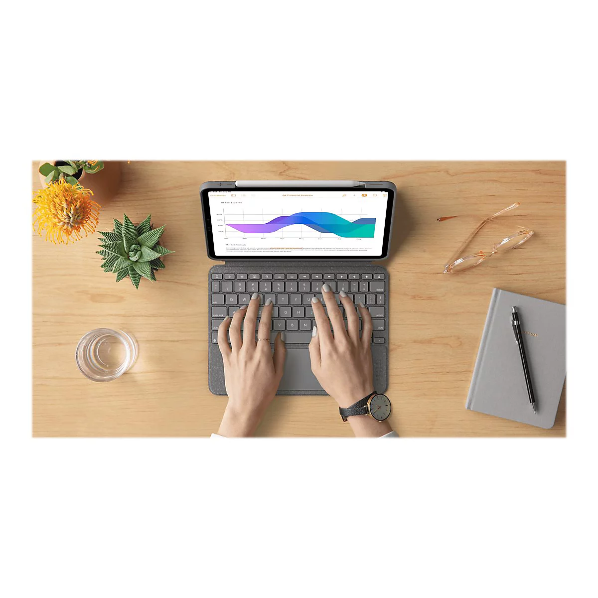 Person tippt auf einer Tastatur. Auf dem Tablet wird ein Diagramm angezeigt. Daneben liegen Brille, Notizbuch und Pflanze.