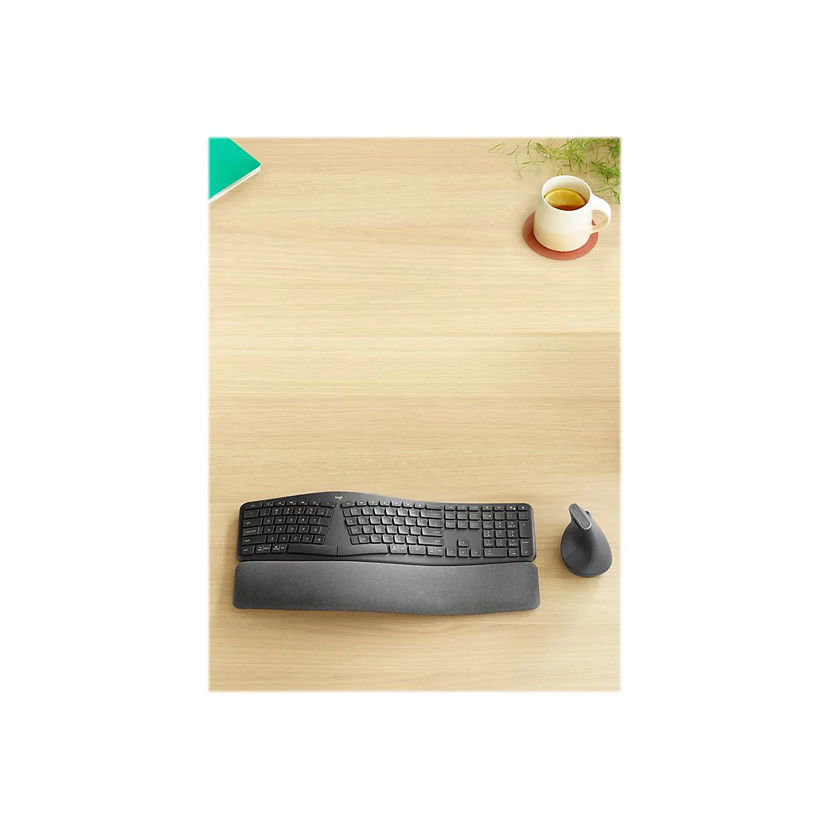 Vue aÃ©rienne d'un clavier et d'une souris ergonomiques sur un bureau en bois. Une tasse de thÃ© et un bloc-notes sont Ã  cÃ´tÃ©.