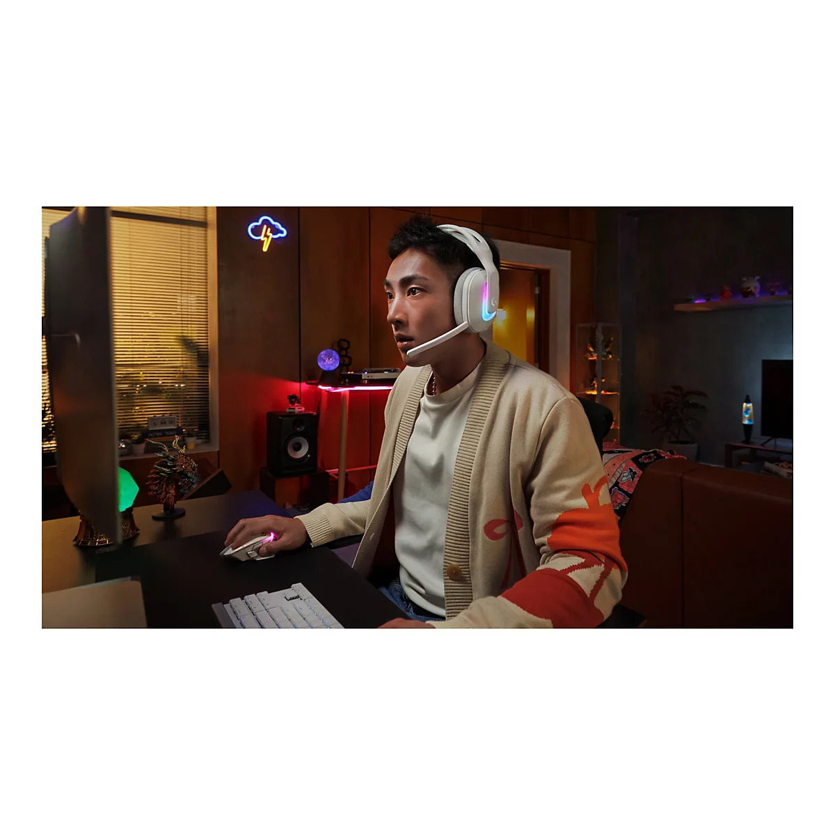 Ein Mann mit weißem Headset sitzt vor einem Computer. Er trägt einen beigen Cardigan und spielt.