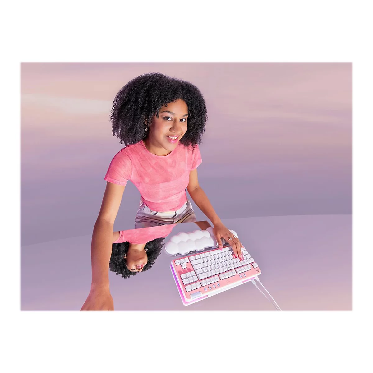 Eine lächelnde Frau mit Locken, rosa Oberteil, an einem Keyboard, das auf einer Oberfläche gespiegelt wird.