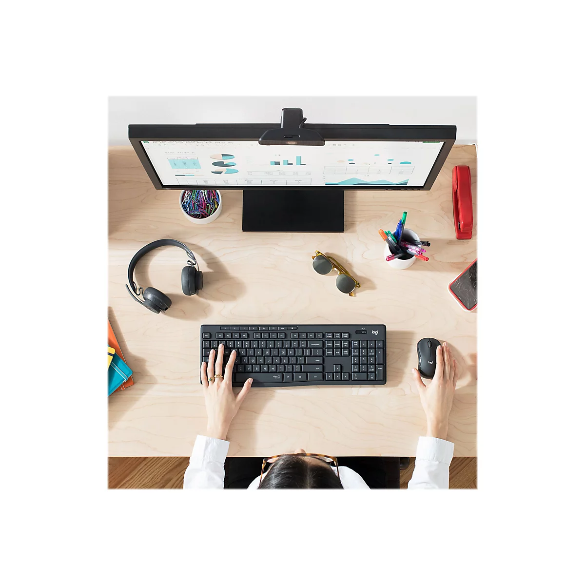 Draufsicht auf Person an einem Schreibtisch mit Computer, Tastatur, Maus, KopfhÃ¶rern und Sonnenbrille. Auf dem Bildschirm Diagramme.