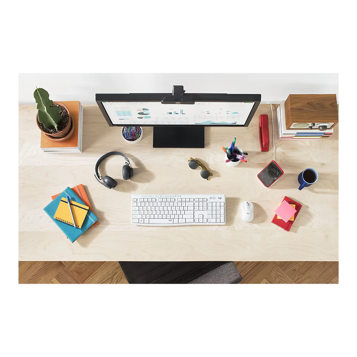 Draufsicht eines Schreibtischs mit Monitor, Tastatur, Maus, KopfhÃ¶rern und diversen BÃ¼roartikeln. Auf dem Monitor sind Diagramme zu sehen.