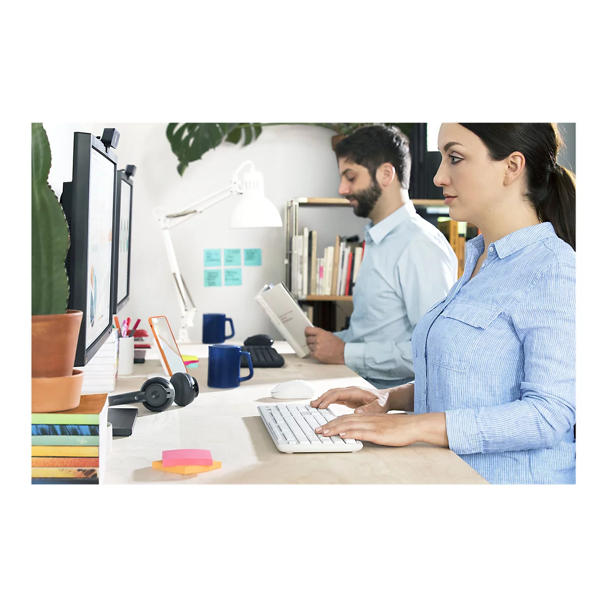 Zwei Personen sitzen an einem Schreibtisch, arbeiten am Computer und lesen Dokumente.