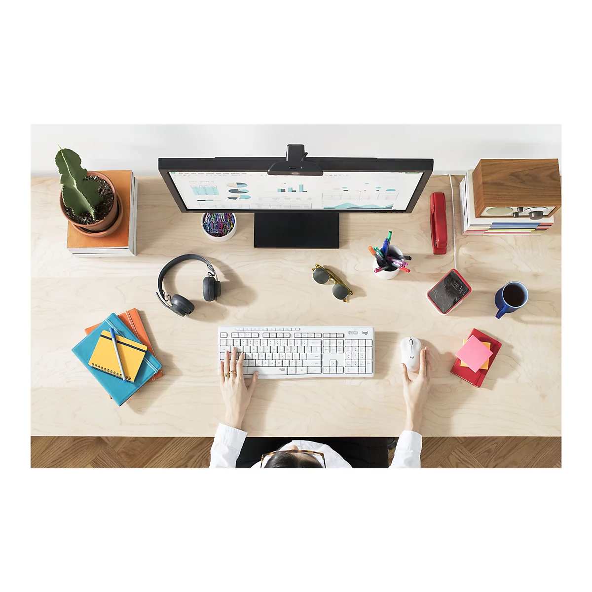 Draufsicht auf einen Schreibtisch, der mit BÃ¼romaterial, Computerbildschirm und HÃ¤nden, die Tastatur und Maus benutzen, ausgestattet ist.
