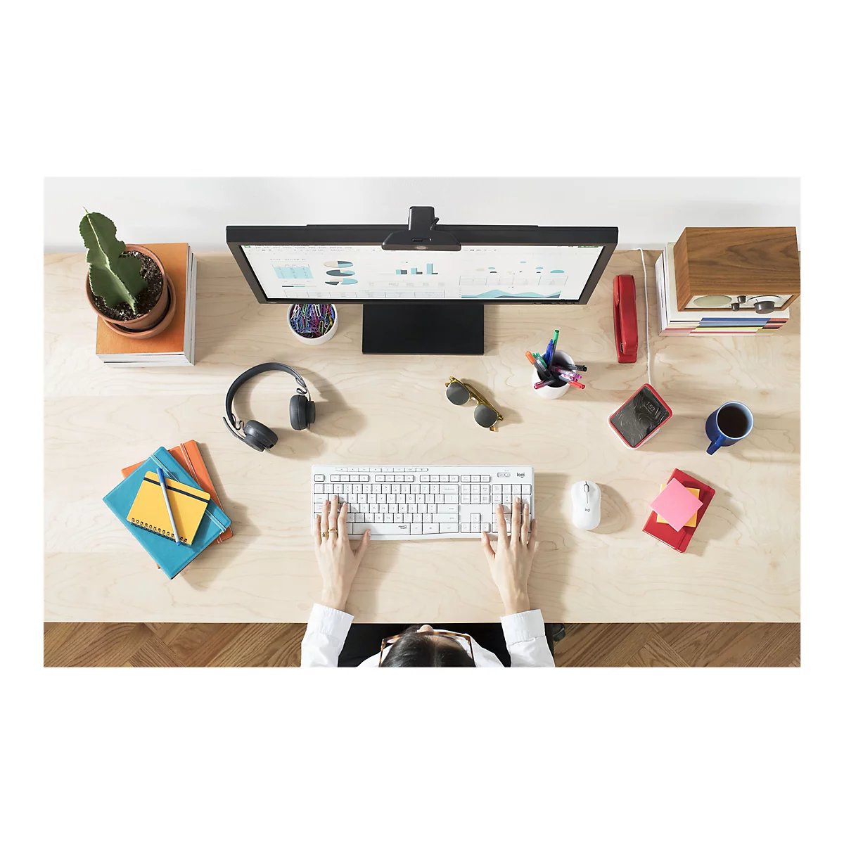 Draufsicht auf einen Schreibtisch mit Computer, Tastatur, Notizblock, KopfhÃ¶rern und den HÃ¤nden einer Person, die tippt.