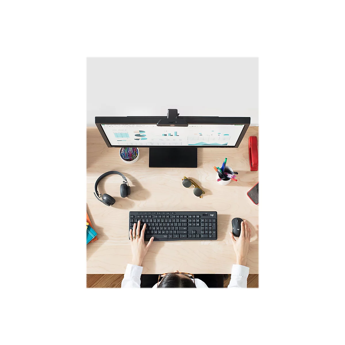 Nahaufnahme einer Person an einem Schreibtisch mit Tastatur, Maus, Monitor und Zubehör. Die Person benutzt die Tastatur.