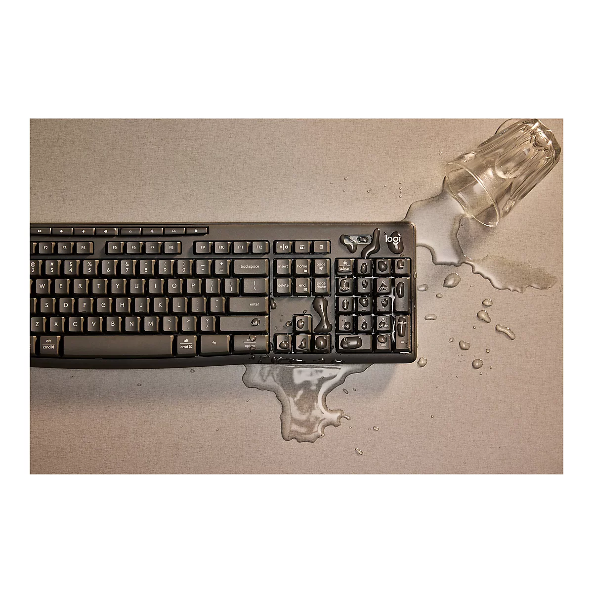 Ein schwarzes Logitech-Keyboard liegt auf einem beigen Untergrund, bedeckt von ausgelaufenem Wasser und einem umgekippten Glas.