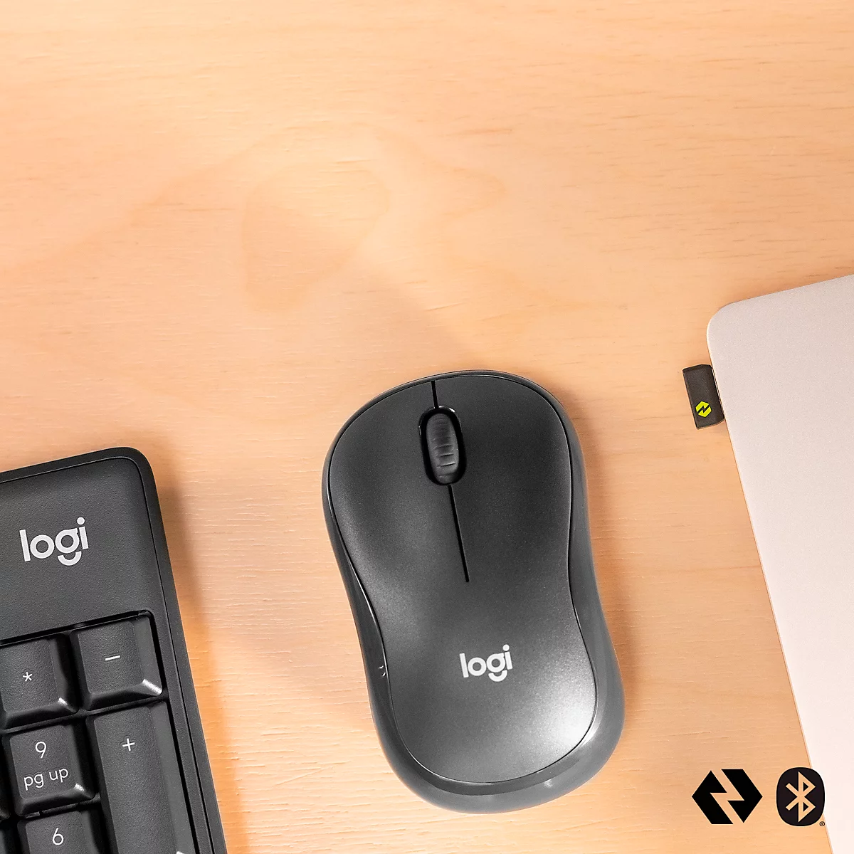 Wireless mouse and number pad by Logitech on light brown wood. A laptop is visible on the right edge.