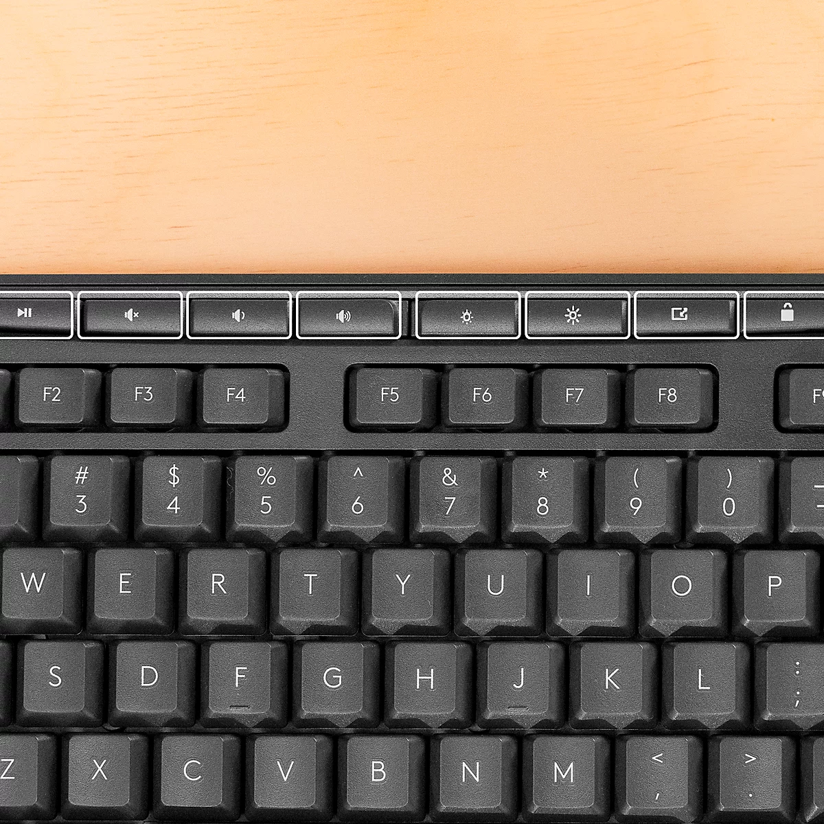 Overhead view of a black keyboard on a wooden surface. Letters, numbers and special characters are clearly visible.