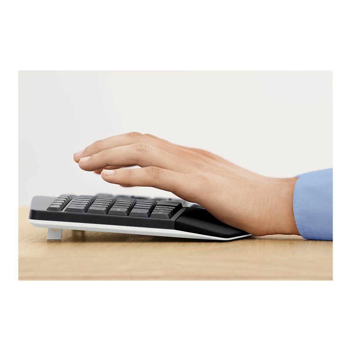 Mains tapant sur un clavier noir avec un repose-paume. En arrière-plan, un champ clair et homogène et une surface en bois.
