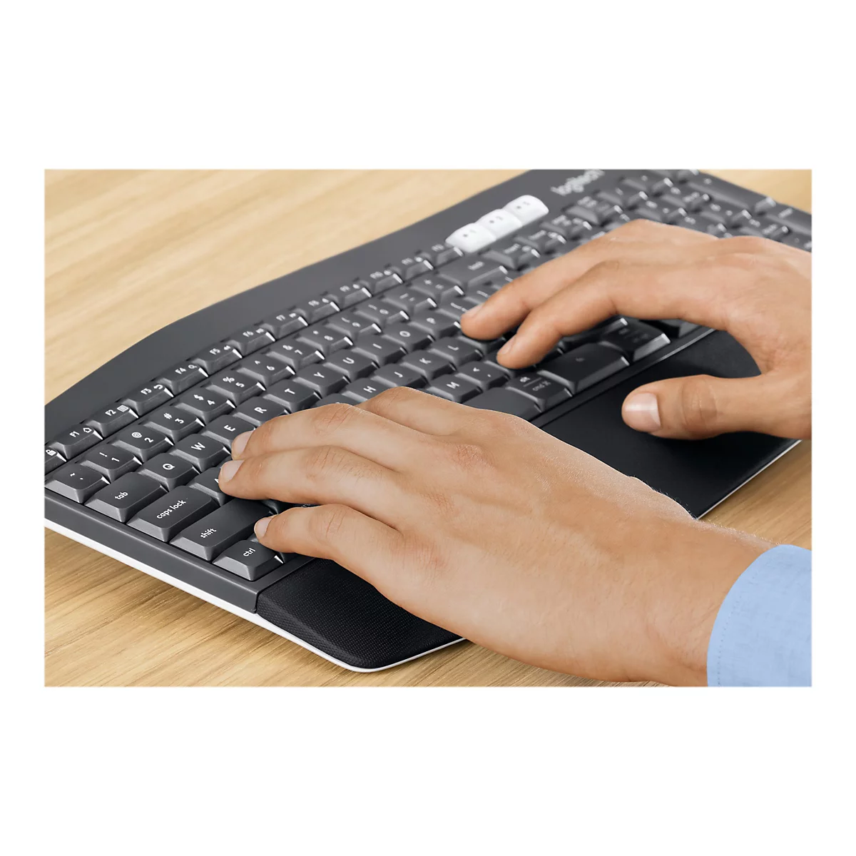 Gros plan d'une personne tapant sur un clavier Logitech sombre ; mains sur les touches, manche bleu en arrière-plan.
