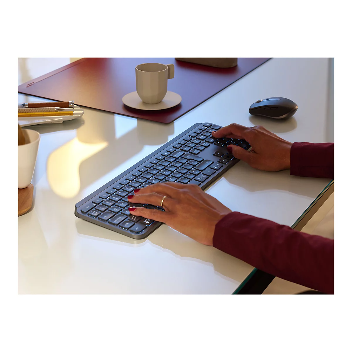 Eine Person tippt auf einer grauen Tastatur. Auf dem Tisch befinden sich eine Tasse, ein Mousepad und eine Maus.