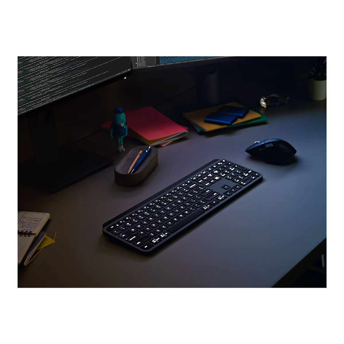 Draufsicht auf eine beleuchtete schwarze Tastatur auf einem Schreibtisch. Neben der Tastatur liegen eine Maus, Notizbücher und dekorative Gegenstände.