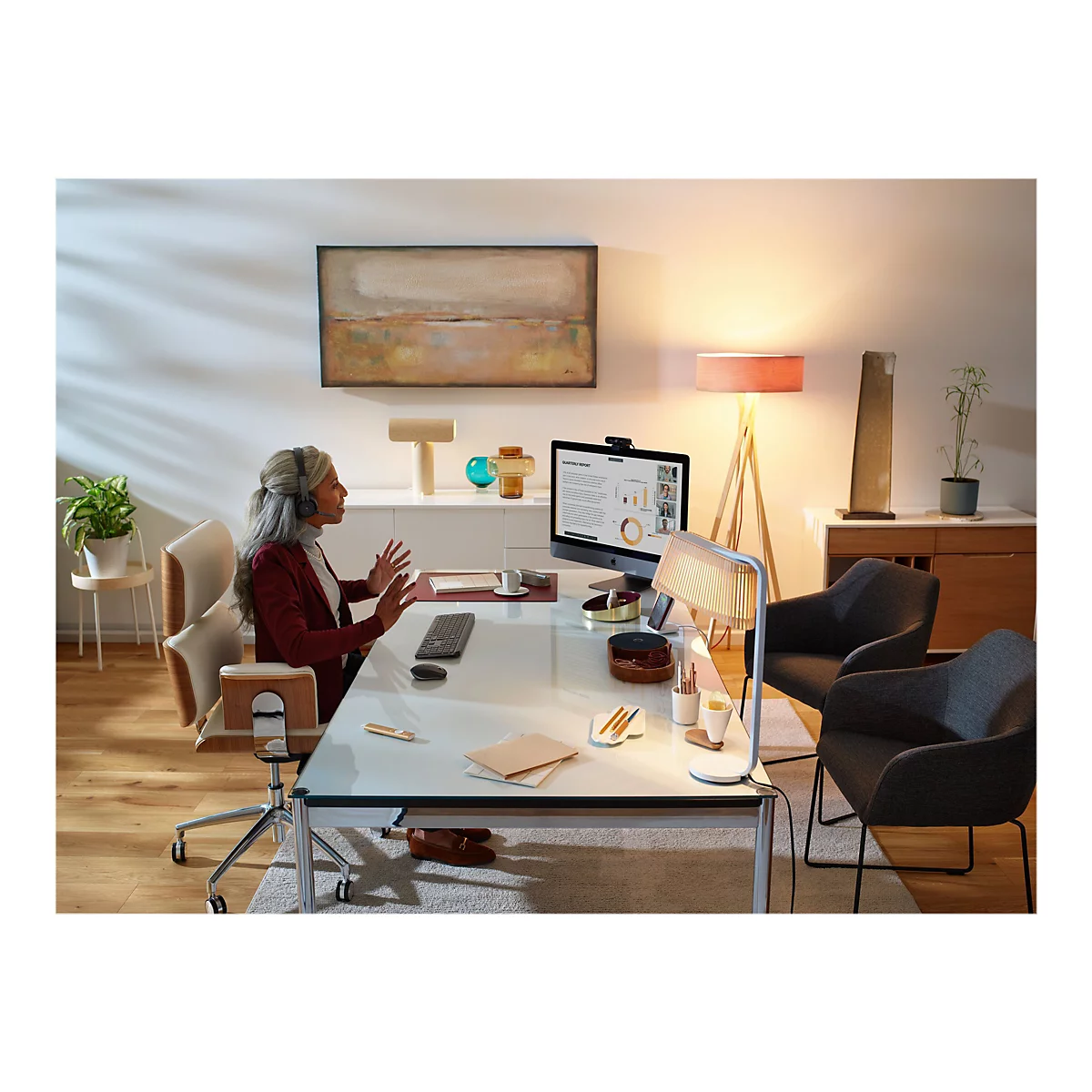 Eine Frau mit Headset nimmt an einem Videoanruf an ihrem Schreibtisch teil. Auf dem Schreibtisch befinden sich ein Monitor, eine Tastatur und verschiedene andere Büroartikel.