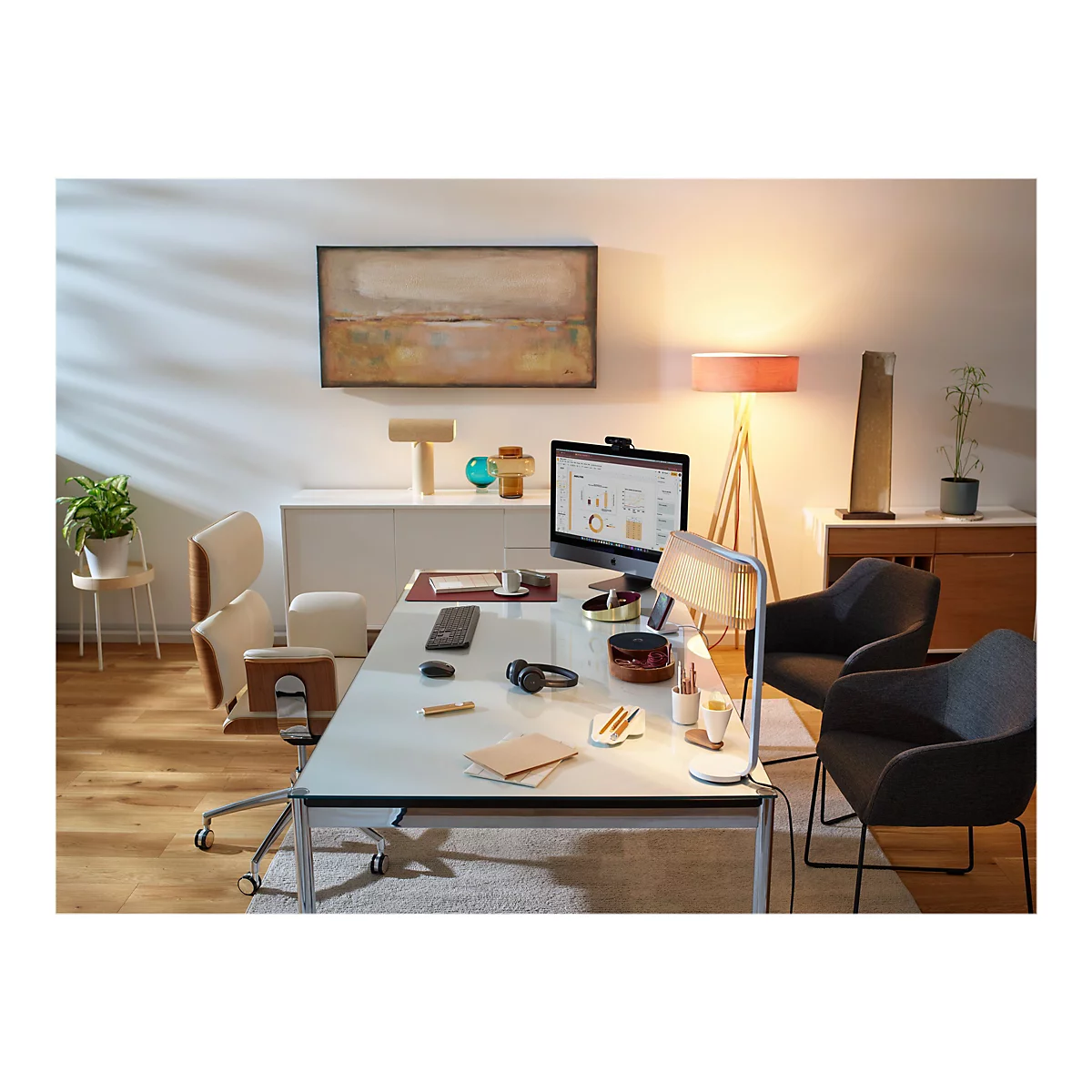 Ein modernes Büro mit Schreibtisch, Monitor, Stuhl und Dekoration. Auf dem Monitor werden Diagramme angezeigt. Auf dem Schreibtisch liegen Kopfhörer, Stifte und Notizen.