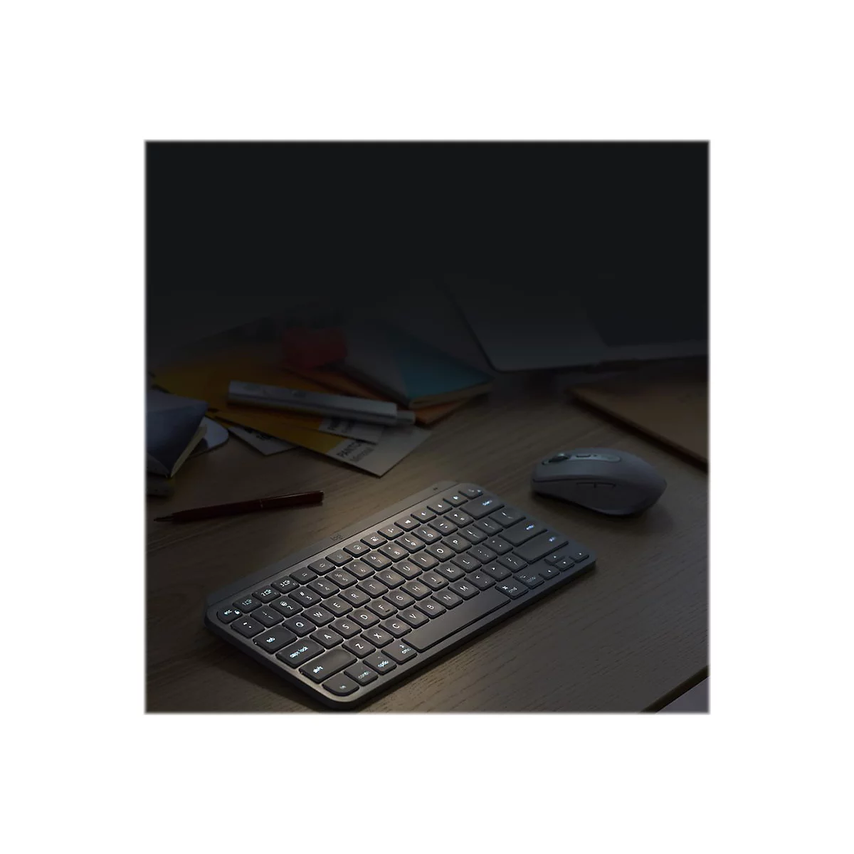 Eine beleuchtete Tastatur und Maus auf einem Holztisch. Im Hintergrund Notizen und ein Laptop.
