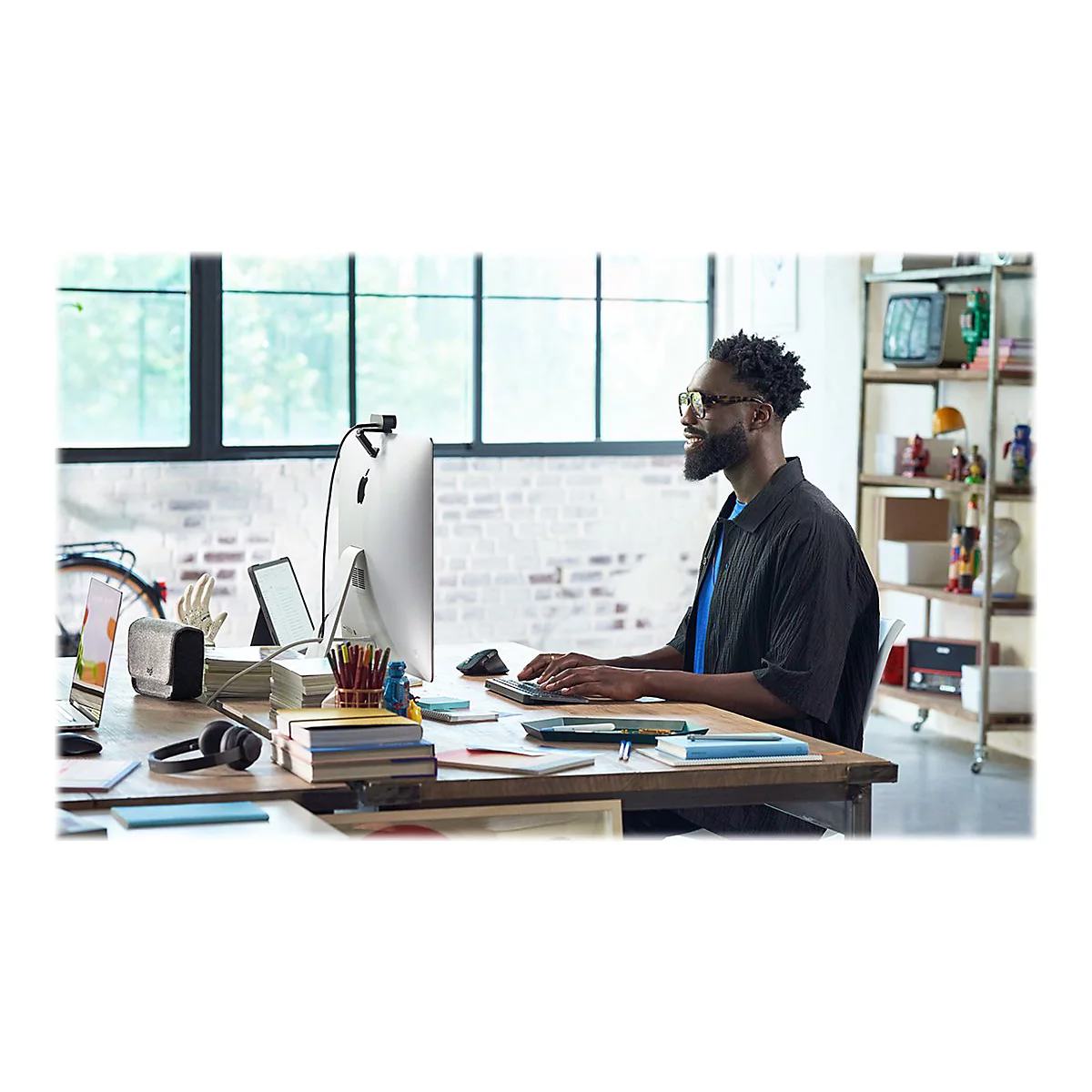 Ein Mann mit Brille sitzt an einem Schreibtisch und arbeitet an einem Computer, mit Mikrofon und Kopfhörern.