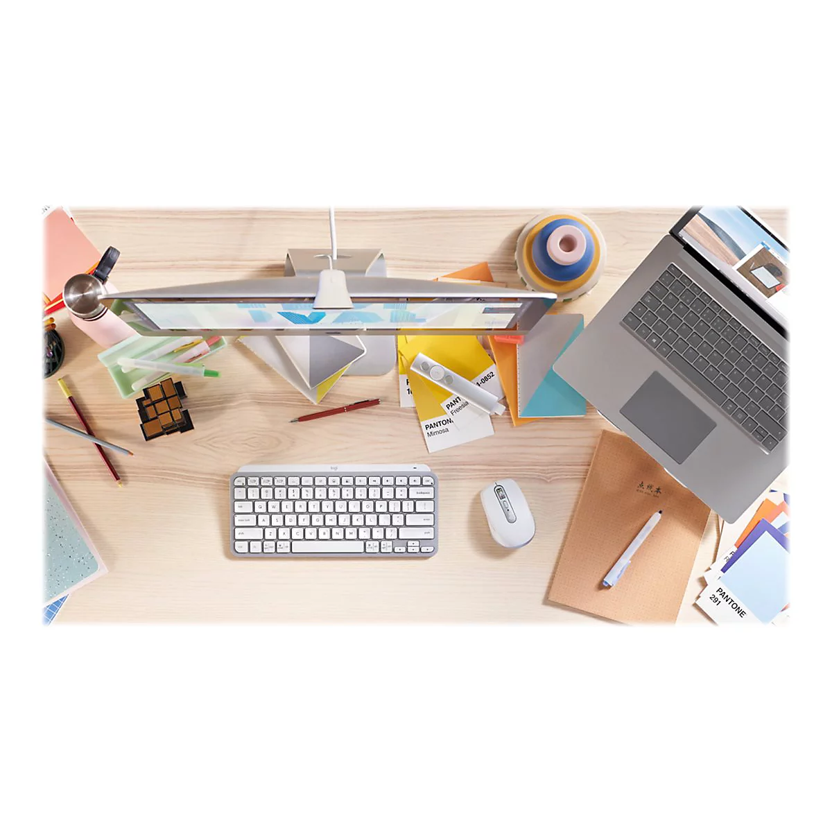 Draufsicht auf einen Schreibtisch mit Computerzubehör, Notizen, Stiften und Laptop. Farben und Texturen sind erkennbar.